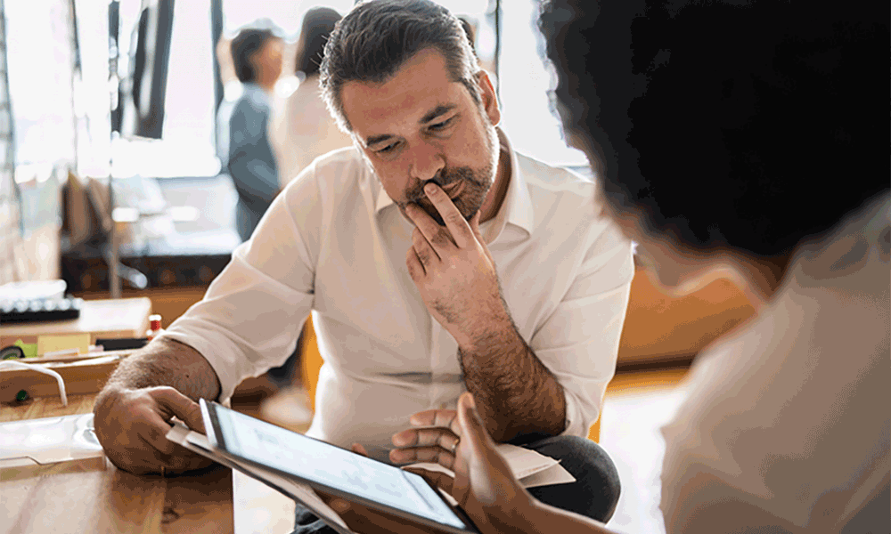 mws-2-2 A man sitting in desk looks to be deep in thought as he looks at a tablet device held by a woman.