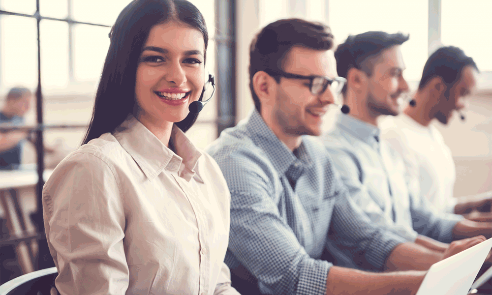 ps-4 A row of four adults sit next to each other in front of computers, each wearing a headset. The female closest to the camera looks at it and smiles.